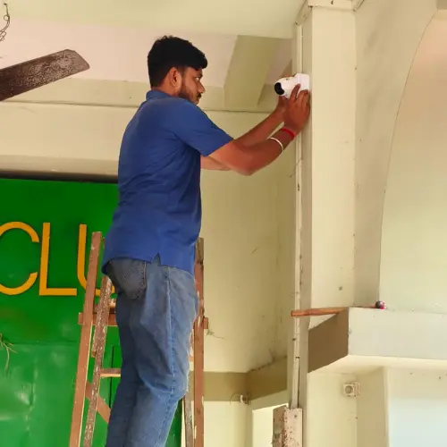 Technician mounting a CCTV camera at a community club entrance in Kolkata